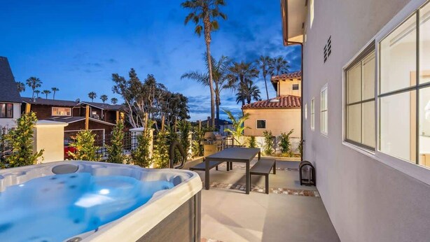 A hot tub in a backyard with a patio, palm trees, and a house in the background. - Modern 2BR Near Beach w/ Parking, Spa, BBQ, EV (San Diego)