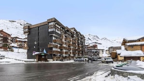 Un hotel a più piani con balconi, una pista da sci sullo sfondo e una strada coperta di neve.