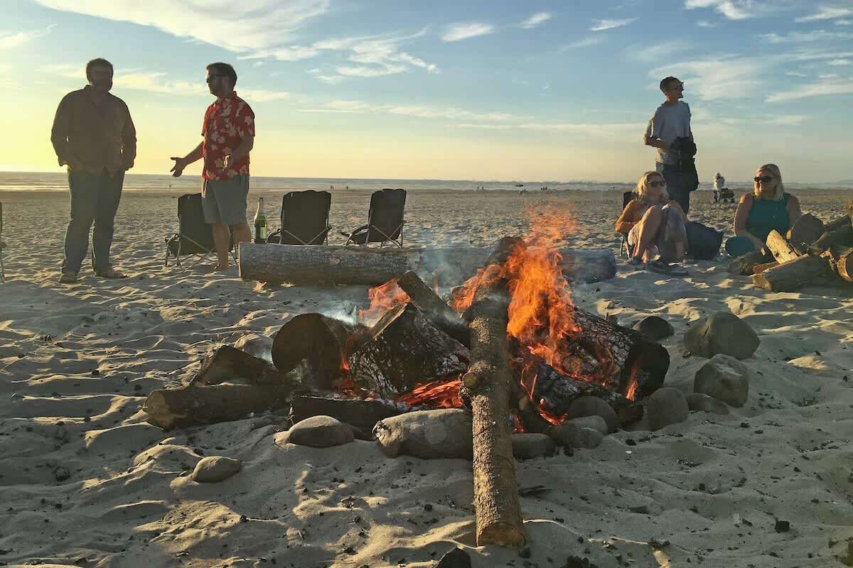 Escena de playa con una fogata y gente alrededor.