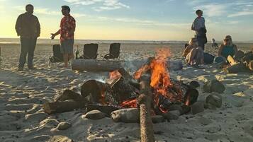 Escena de playa con una fogata y gente alrededor.