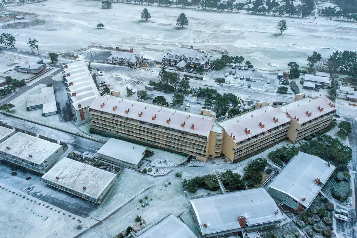 Vista aérea de un complejo de edificios grande con varias construcciones, áreas de estacionamiento e infraestructura circundante.