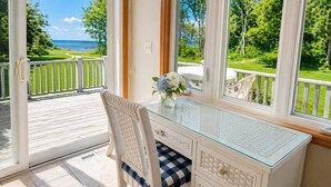 Une pièce avec un bureau en verre, une chaise en osier, une vue sur la mer et une rambarde blanche.