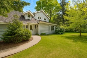 A two-story house with a covered porch, a well-maintained lawn, and mature trees. - Waterfront Home|Dock & Kayaks|5 Min to Baileys Harbor (Baileys Harbor)
