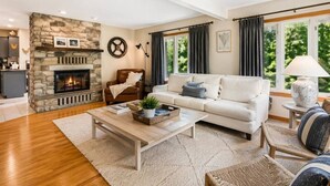 Un salon avec une cheminée en pierre, un canapé, une table basse et une vue sur la verdure à l’extérieur.