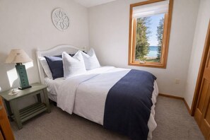 A bedroom with a bed, a nightstand, a lamp, a decorative wall piece, and a window with a view. - Waterfront Home|Dock & Kayaks|5 Min to Baileys Harbor (Baileys Harbor)