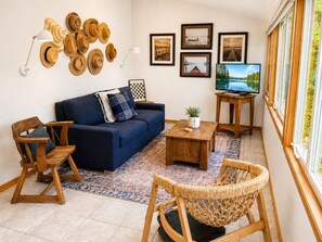 A living room with a blue sofa, wooden chairs, a coffee table, and a TV on a stand. - Waterfront Home|Dock & Kayaks|5 Min to Baileys Harbor (Baileys Harbor)