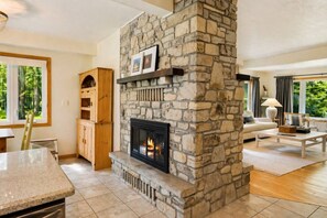 A stone fireplace with a mantel, a wooden cabinet, a dining area, and a living room with a sofa and a lamp.