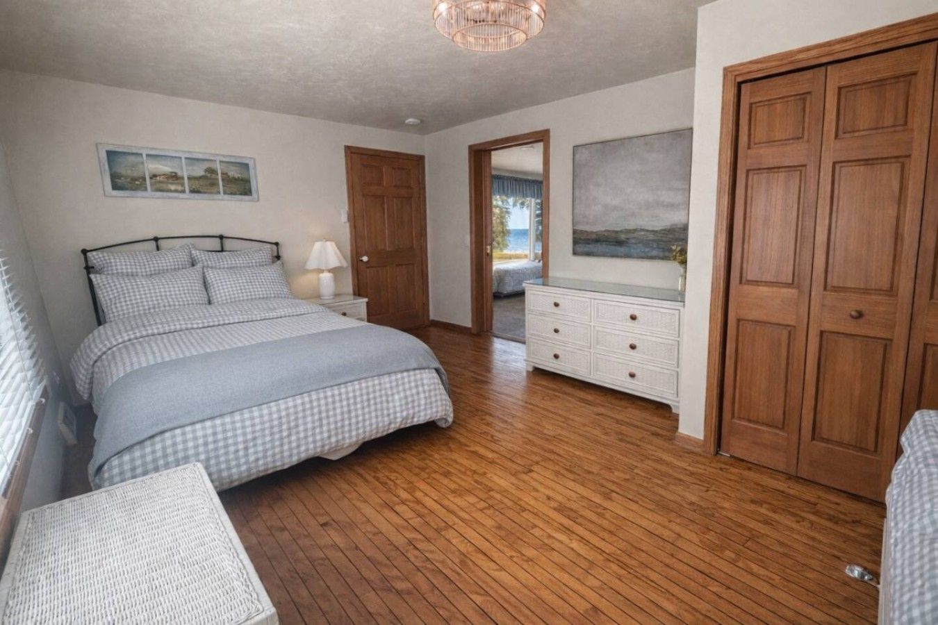 A bedroom with a bed, a dresser, a nightstand, and a door leading to another room.