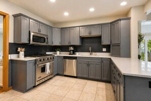 A modern kitchen with grey cabinets, stainless steel appliances, and a large island. - Waterfront Home|Dock & Kayaks|5 Min to Baileys Harbor (Baileys Harbor)