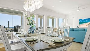 A dining area with a table set for four, a vase with flowers, and a view of the ocean.