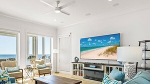 A spacious living room with a large window overlooking the ocean, a fireplace, and a ceiling fan.