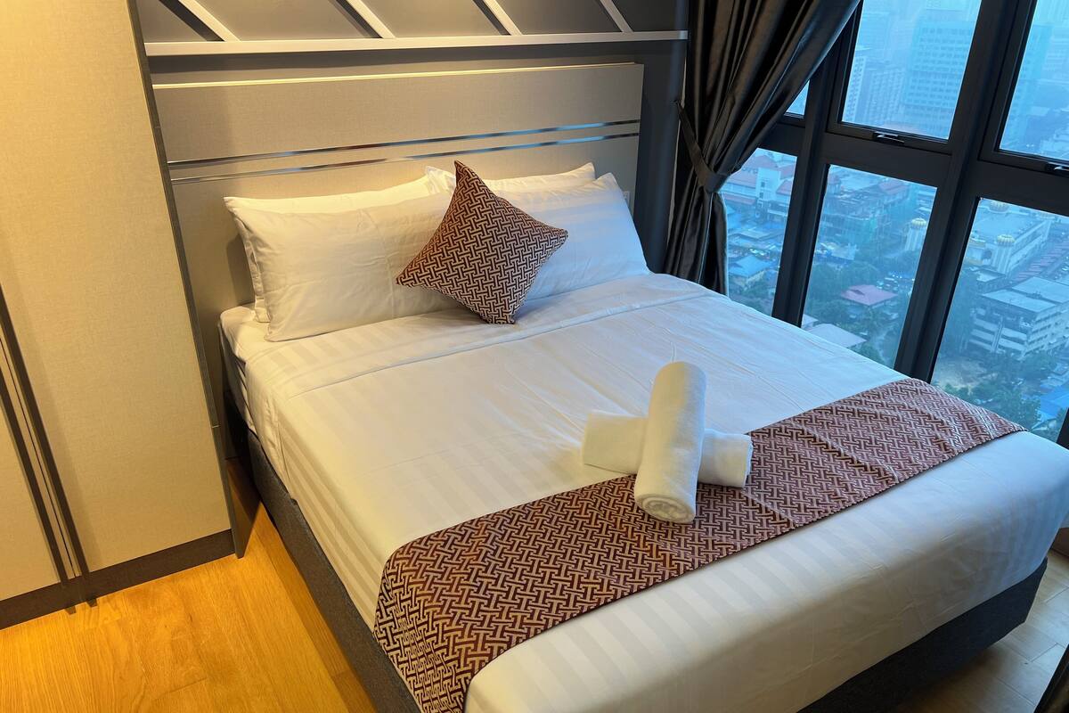 Une chambre d’hôtel avec un lit, un plaid à motifs et une vue sur la ville grâce à de grandes fenêtres.