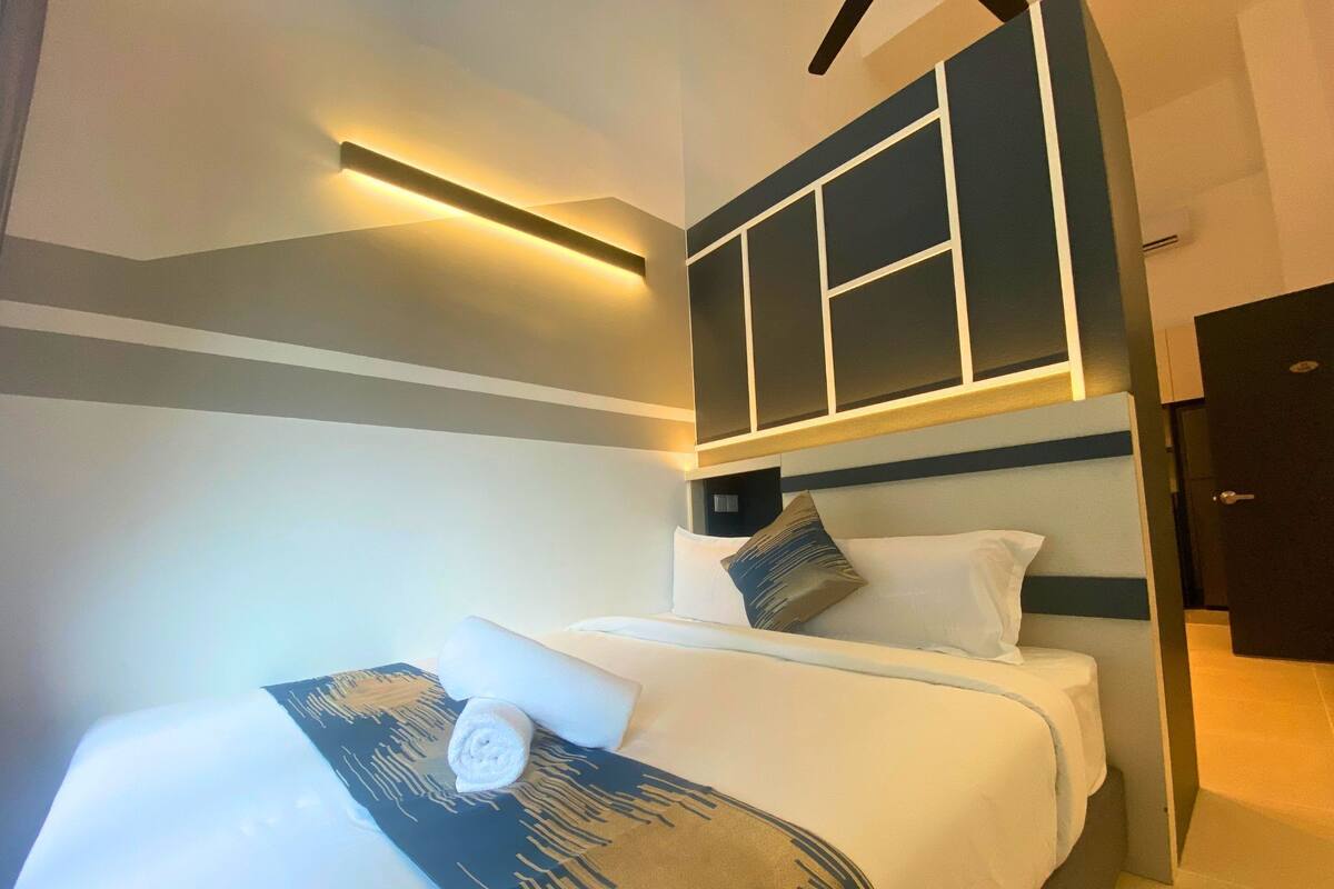 Une chambre d’hôtel moderne avec un lit soigneusement fait, une tête de lit dotée d’un éclairage intégré et une porte située à droite.