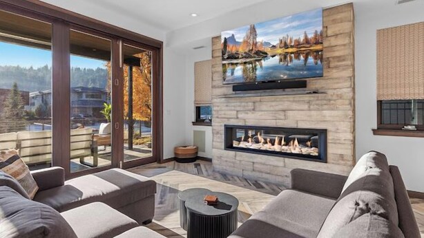 A modern living room with a large TV, fireplace, and a scenic view through the glass door. - Bellerive Gem (Coeur d'Alene)