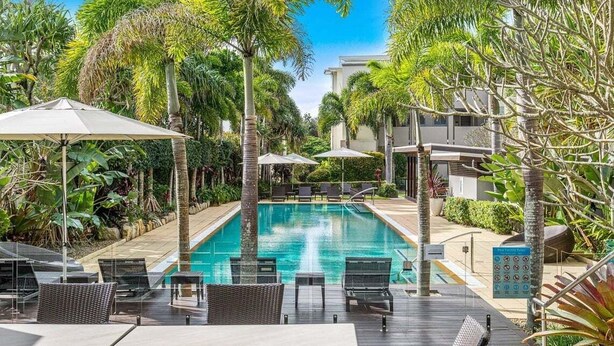A poolside area with lounge chairs and umbrellas, surrounded by tropical plants and a clear blue sky. - Palm Horizon -3B Bali Resort in Kingscliff (1218) (Tweed)