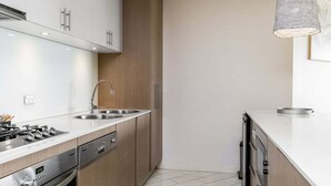 A modern kitchen with stainless steel appliances, wooden cabinets, and a hanging pendant light. - Palm Horizon -3B Bali Resort in Kingscliff (1218) (Tweed)