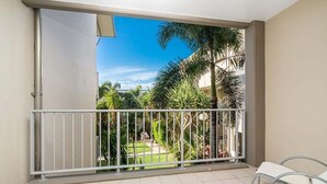 A balcony with a metal railing, a view of a garden with palm trees, and two white chairs. - Palm Horizon -3B Bali Resort in Kingscliff (1218) (Tweed)
