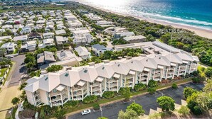 An aerial view of a coastal residential area with a large building complex, Ap 1218 Bale, featuring multiple balconies and a parking lot. - Palm Horizon -3B Bali Resort in Kingscliff (1218) (Tweed)