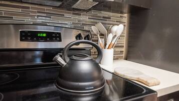 A kitchen with a stainless steel oven, a black electric kettle, and a white utensil holder on the counter.