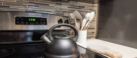 A kitchen with a stainless steel oven, a black electric kettle, and a white utensil holder on the counter.