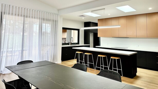 A modern kitchen with a central island, black bar stools, and a dining table with chairs. - Emmylou Escape - Sleeps 16 (Moama)