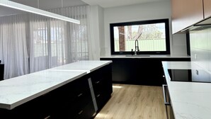 A modern kitchen with a large island, pendant lighting, a window with a view, and built-in appliances. - Emmylou Escape - Sleeps 16 (Moama)