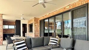 An outdoor patio with a brick wall, a ceiling fan, and a dining area with a table and chairs. - Emmylou Escape - Sleeps 16 (Moama)