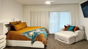 A bedroom with a bed, a chair, a ceiling fan, and a large window with curtains. - Emmylou Escape - Sleeps 16 (Moama)