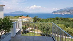 A balcony with a view of the sea, a mountain in the distance, and a white building with a red roof. - Maison Regina Giovanna (Sorrento)
