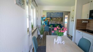 Ein Essbereich mit einem Tisch mit der Aufschrift "Mein" und einer Vase voller pinker Tulpen. Es gibt Stühle, einen Fernseher und ein Bild an der Wand.