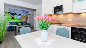Eine moderne Küche mit weißen Schränken, einer Mikrowelle und einem Backofen. Auf dem Esstisch steht eine Vase mit rosa Tulpen.
