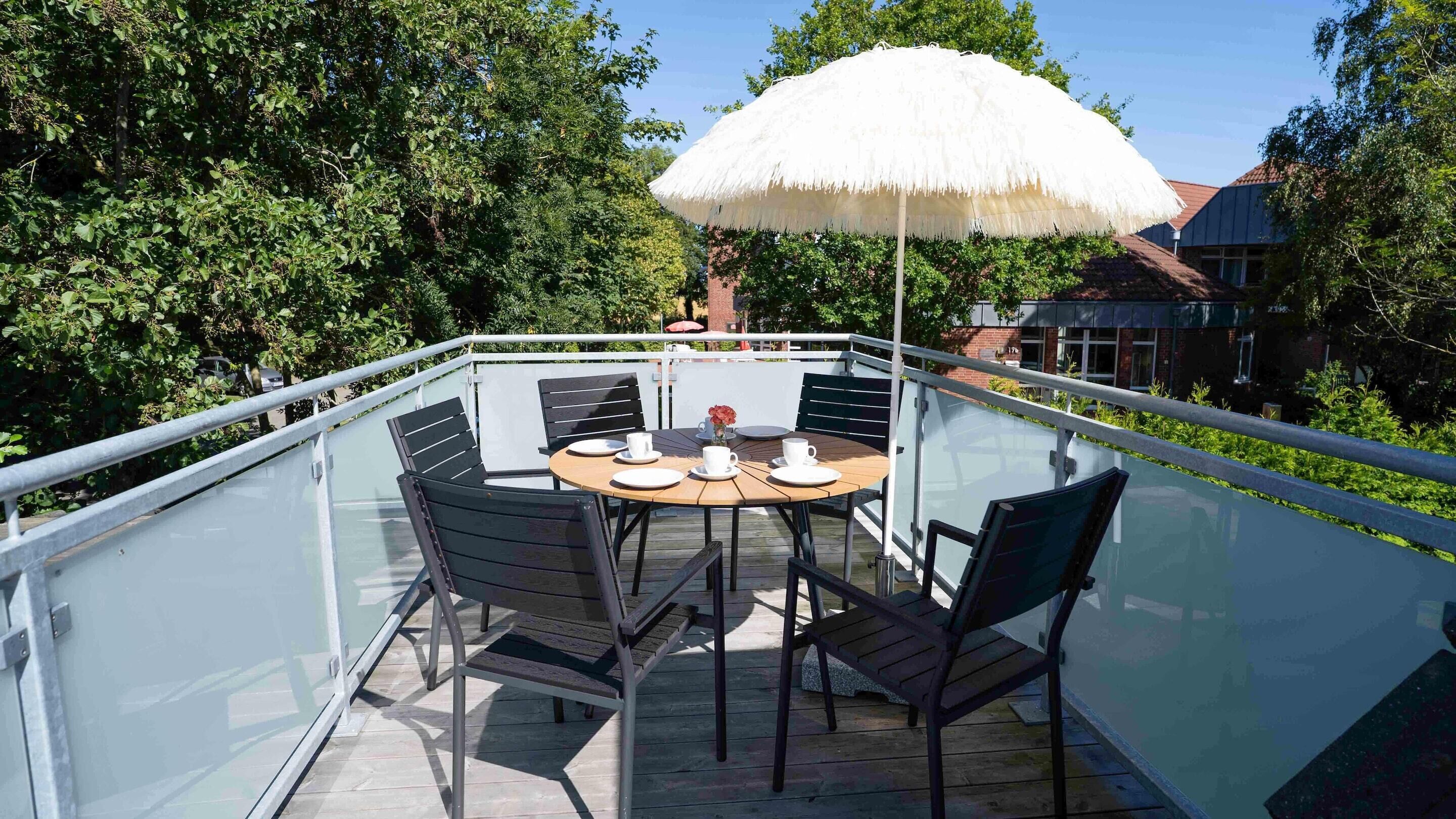 A glass-enclosed outdoor dining area with a round table, chairs, and a large umbrella.