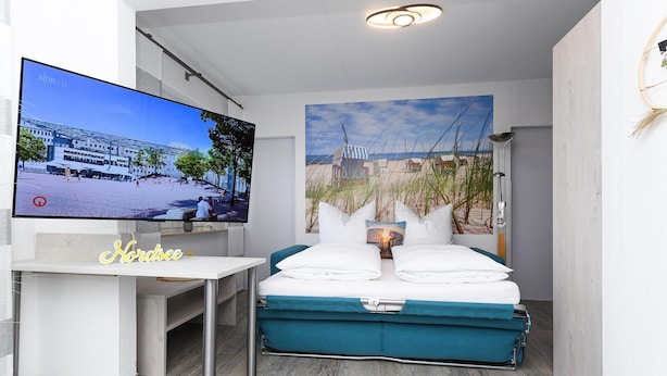 Ein modernes Hotelzimmer mit einem Bett, einem Fernseher und einem Bild mit einer Strandansicht.