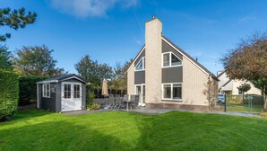 A two-story house with a well-maintained lawn and a small shed. - Charming Villa Near the sea and Forest (De Koog)