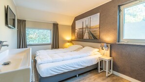 A modern bedroom with a large bed, a bedside table, a nightstand, a wall-mounted TV, a window with curtains, and a painting on the wall. - Charming Villa Near the sea and Forest (De Koog)