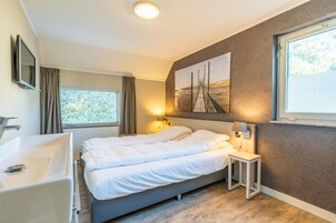 Un dormitorio moderno con una cama grande, una mesita de noche, un televisor montado en la pared, una ventana con cortinas y un cuadro en la pared.