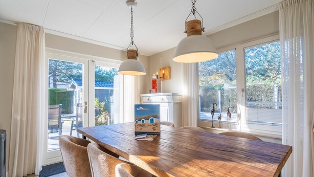 A dining area with a wooden table, beige chairs, and pendant lights. - Charming Villa Near the sea and Forest (De Koog)