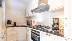 A modern kitchen with white cabinets, a gas stove, an oven, and a coffee maker. - Charming Villa Near the sea and Forest (De Koog)