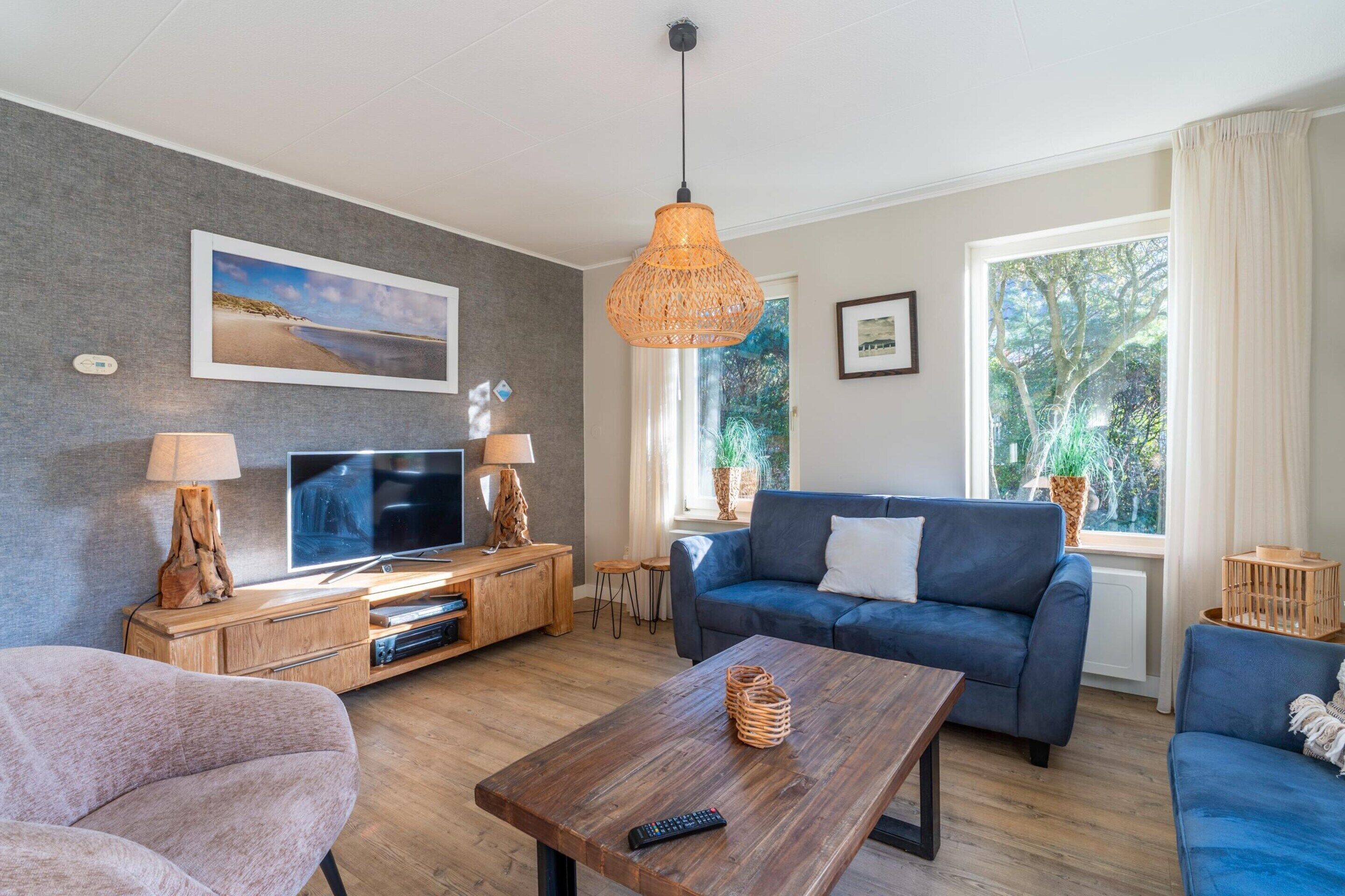A modern living room with a large TV, a blue sofa, a wooden coffee table, and a wicker lamp.