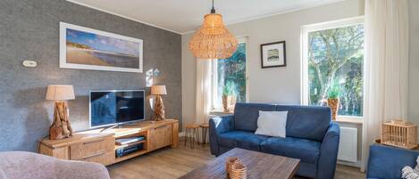 A modern living room with a large TV, a blue sofa, a wooden coffee table, and a wicker lamp.