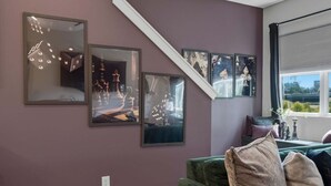 A room with a green sofa, a staircase, and wall-mounted artwork. - Rooftop Views, 4BR 4BA, 7 Beds, Near Broadway! (Nashville)
