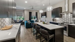 A modern kitchen with a central island, bar stools, a ceiling fan, pendant lights, and a built-in stove. - Rooftop Views, 4BR 4BA, 7 Beds, Near Broadway! (Nashville)