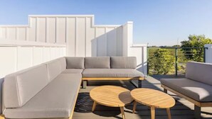 A modern outdoor seating area with a grey sectional sofa and two round wooden tables. - Rooftop Views, 4BR 4BA, 7 Beds, Near Broadway! (Nashville)