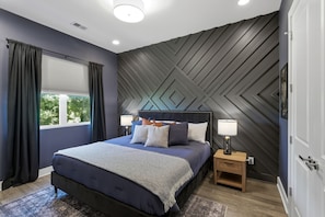 A bedroom with a bed, nightstands, a window with curtains, and a wall with a geometric pattern.