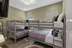 A bunk bed room with two beds, a television, and a window with blinds.