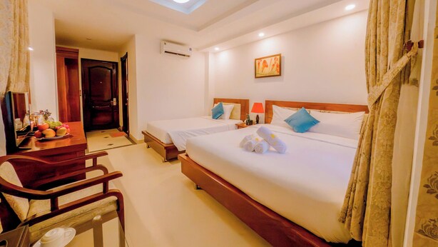 A hotel room with two beds, a desk with a chair, a small table with a lamp, and a ceiling light. - Lanxy Nha Trang (Nha Trang)