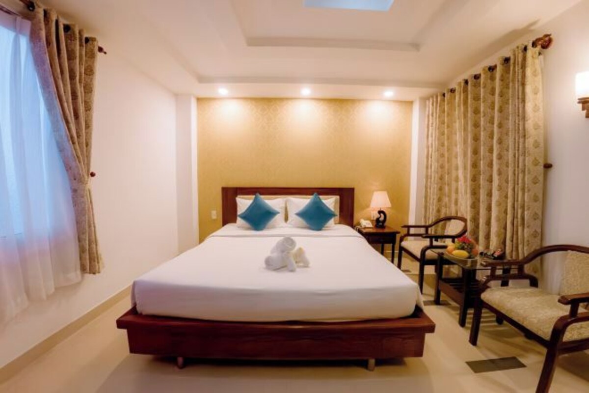 Une chambre d’hôtel avec un lit, une table de chevet, une chaise et une table sur laquelle se trouve un panier de fruits.