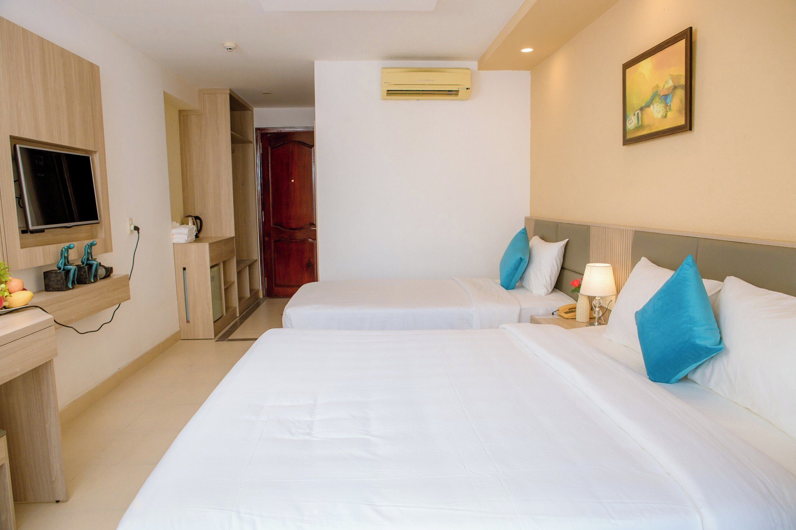 A hotel room with two beds, a TV, a desk, and a painting on the wall.