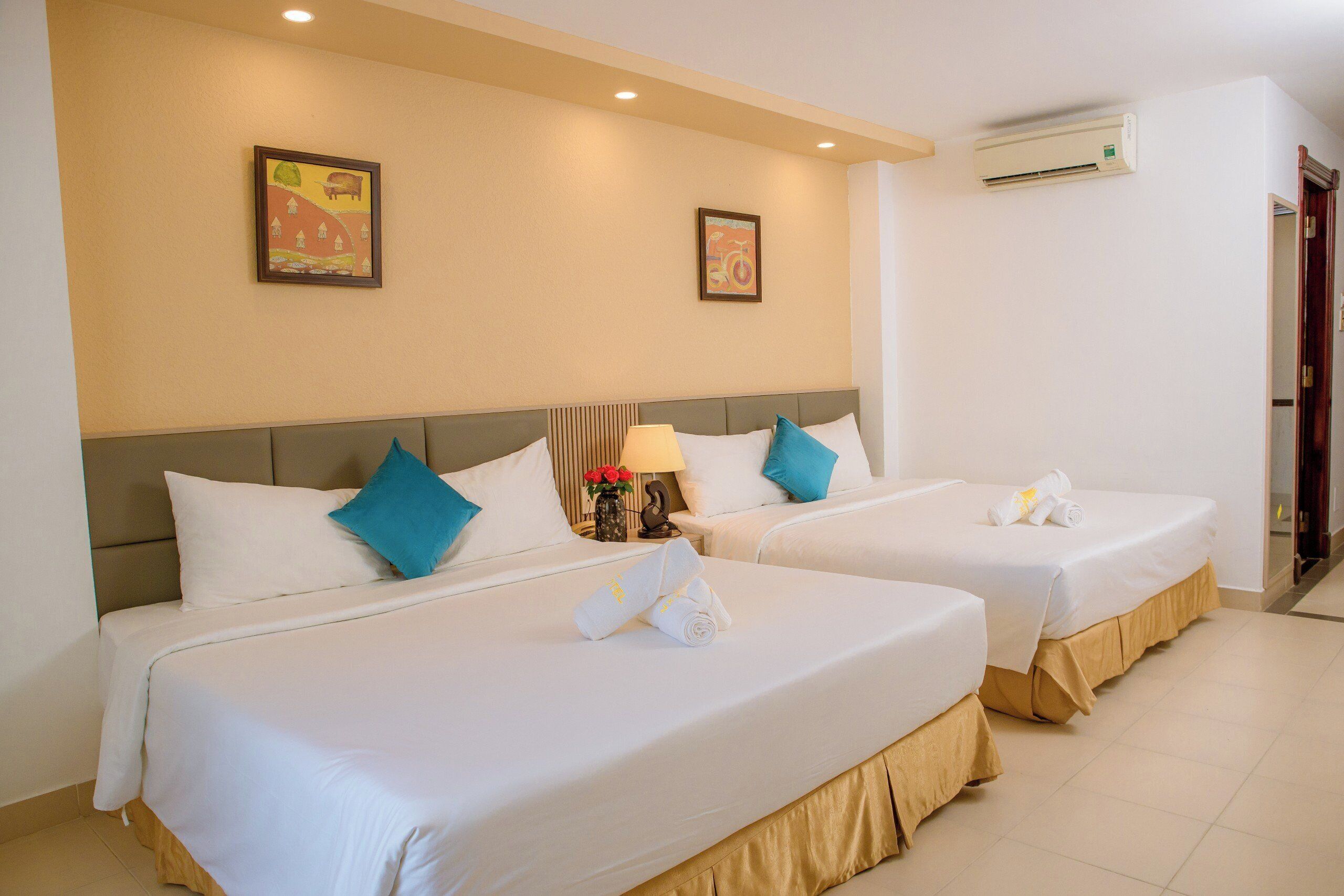 A hotel room with two beds, beige walls, and a ceiling fan.