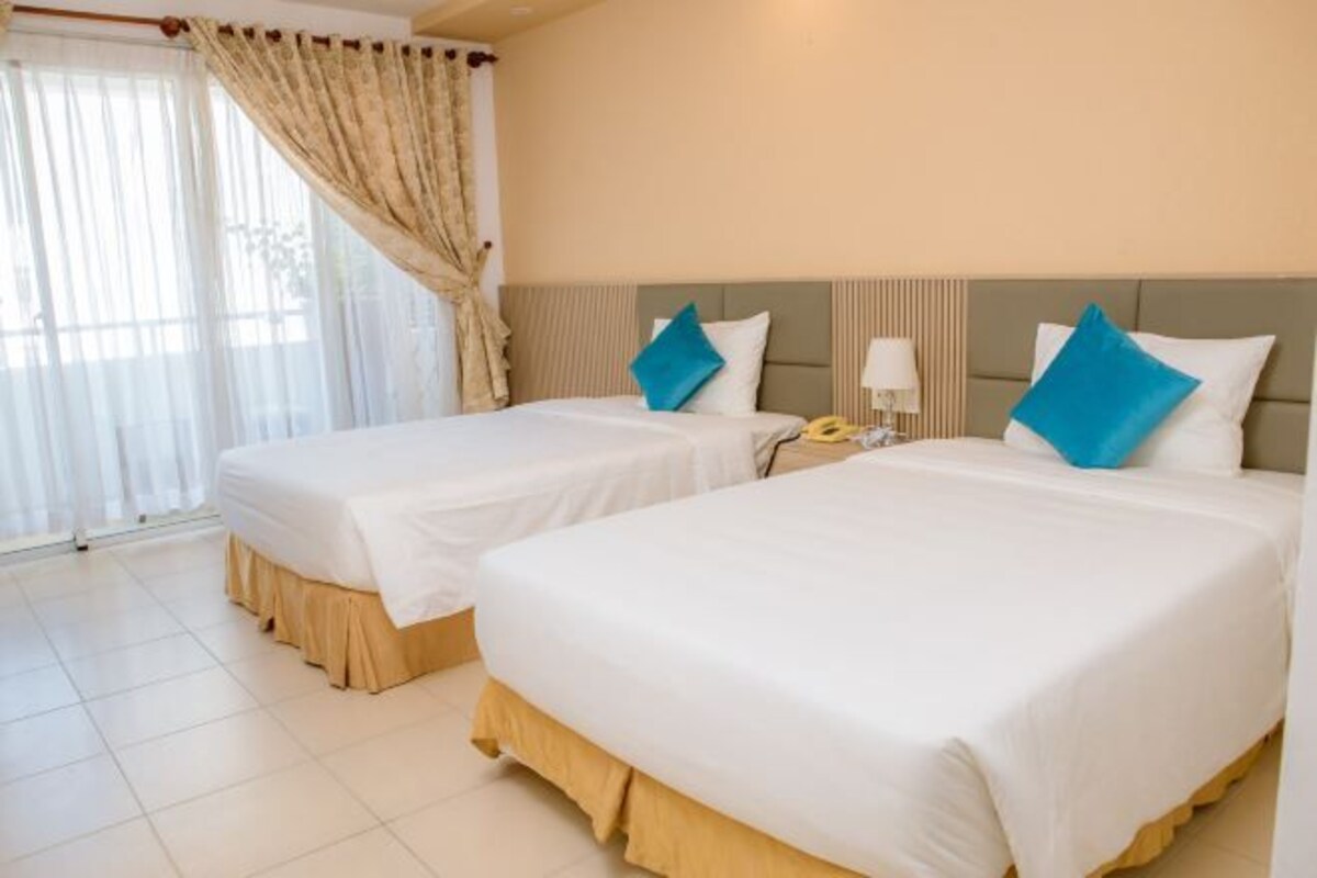 Une chambre d’hôtel avec deux lits, des rideaux beiges et une fenêtre ornée de rideaux blancs et légers.